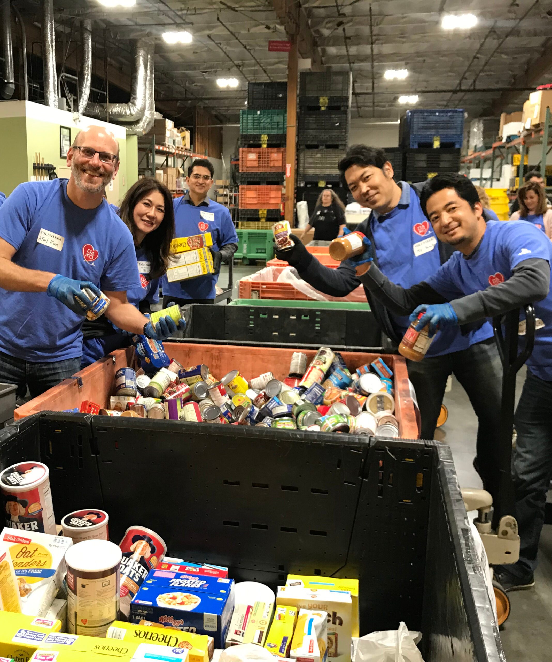 PlayStation Cares Team shown filling boxes for a food drive in a large warehouse.
