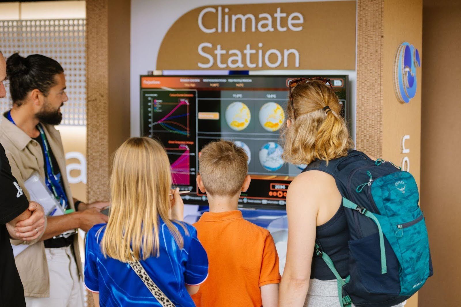 Climate Stationアプリのディスプレイを囲む子供たちと大人たち。画面には地球儀の画像やグラフが表示されている。