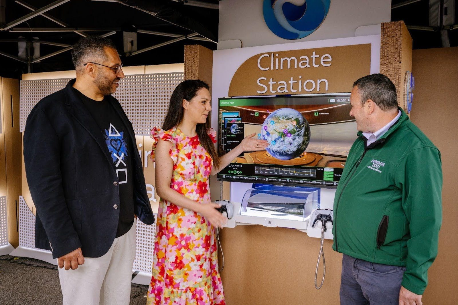 Climate Stationアプリの展示の周りに集まった女性と2人の男性。女性は地球の画像を表示している画面を指差している。