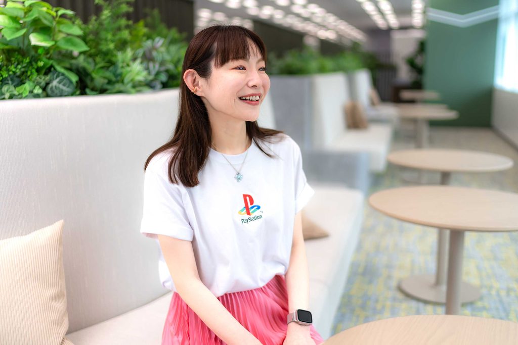 オフィスのラウンジで、白いTシャツの社員が笑顔で座っている