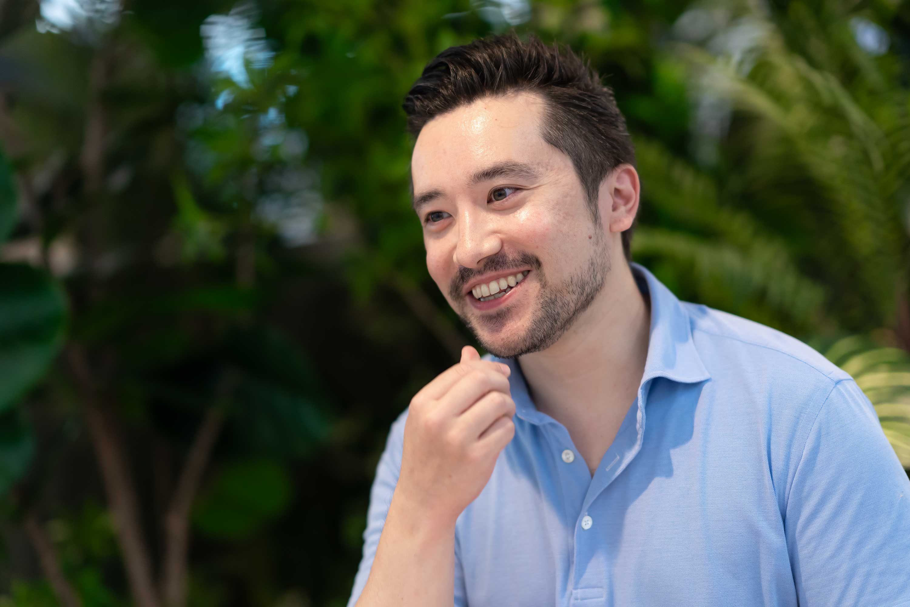 緑に囲まれた空間で、青いシャツの社員が笑顔で話している