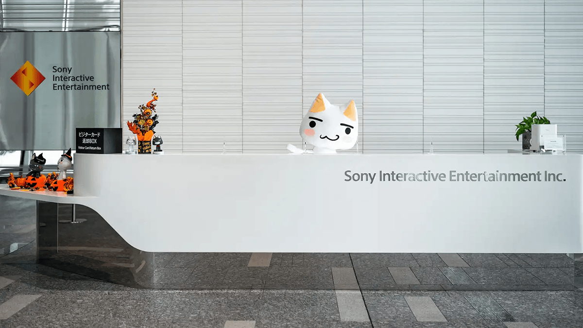 ソニー・インタラクティブエンタテインメントの受付でカメラに向かって手を振っている白猫のキャラクター、トロ