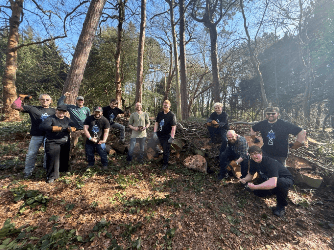 「The Friends of Tower Hamlets Cemetery Park」の森の中で、作業用手袋やPlayStationロゴTシャツを着用し、ポーズをとるSIEのボランティアスタッフグループの写真。