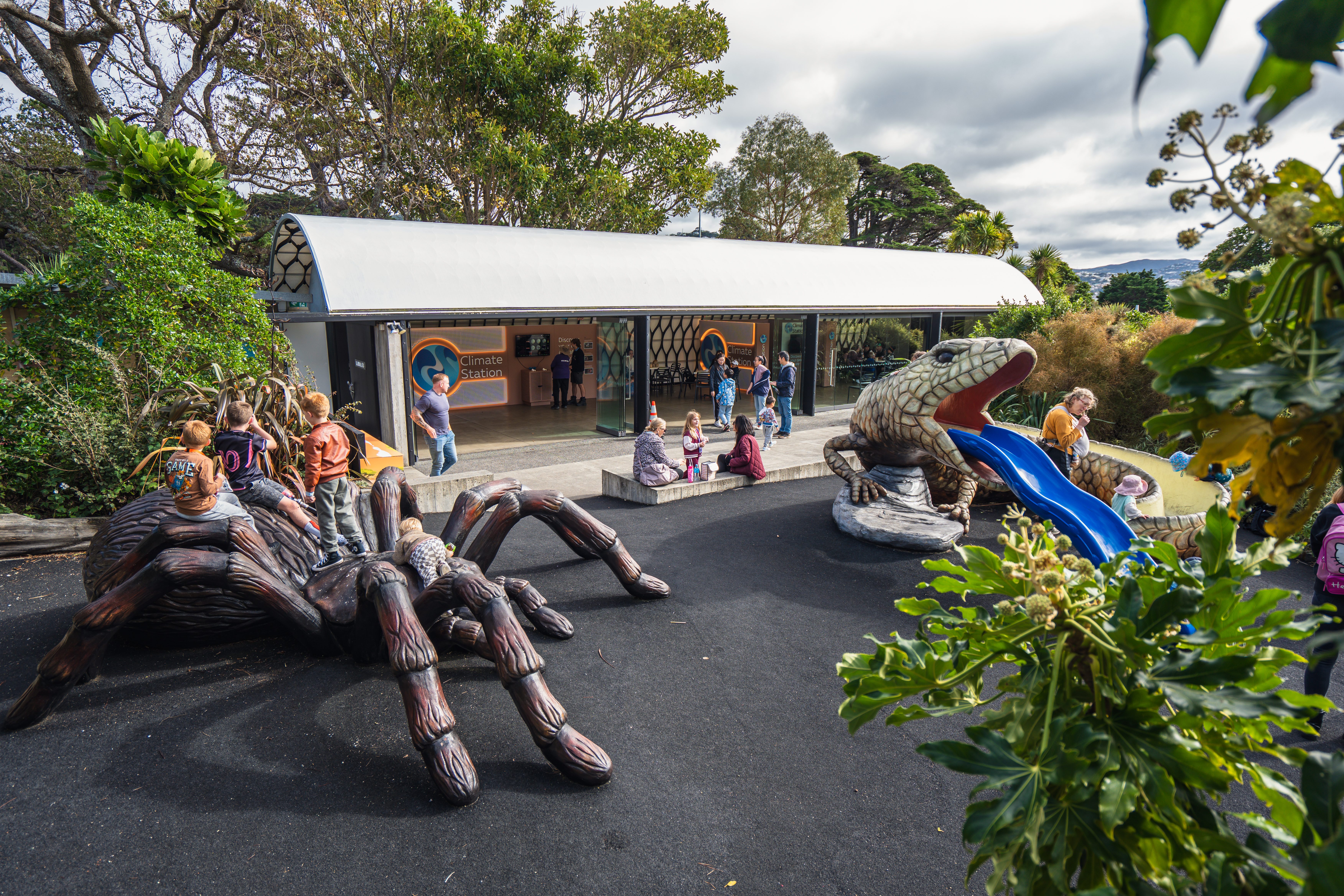 ウェリントン動物園の「Climate Station」展示会場の全景。屋外には巨大なクモやトカゲの滑り台の遊具があり、子どもたちや来訪者で賑わっている写真。