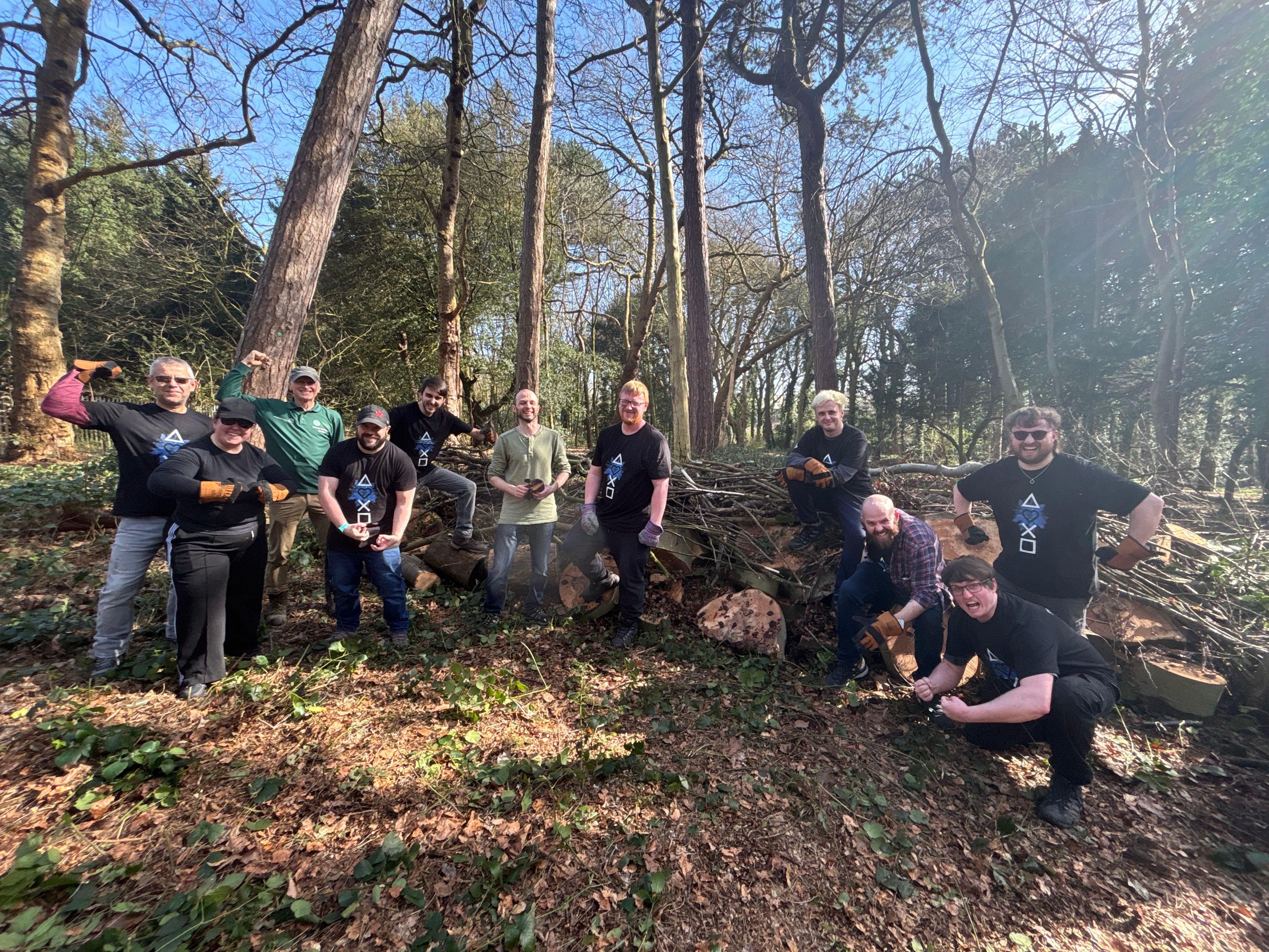 「The Friends of Tower Hamlets Cemetery Park」の森の中で、作業用手袋やPlayStationロゴTシャツを着用し、ポーズをとるSIEのボランティアスタッフグループの写真。